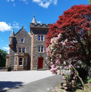 an old castle with a red tree in front of it at Machermore Castle in Newton Stewart