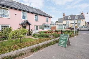 ein Schild vor einem rosa Haus mit Garten in der Unterkunft Coachman's Cottage, Wrentham in Beccles