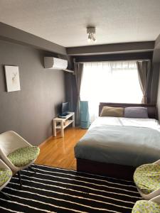 1 Schlafzimmer mit einem Bett, 2 Stühlen und einem Fenster in der Unterkunft SONIC APARTMENT HOTEL in Dazaifu