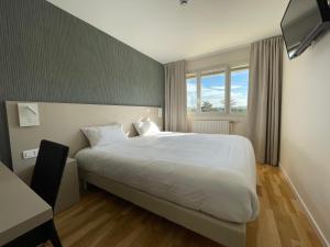 a bedroom with a white bed and a desk and window at Hôtel Valpré in Écully