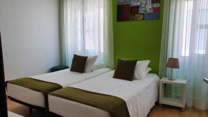 two beds in a room with green walls and windows at Hotel Palmeira in Aveiro