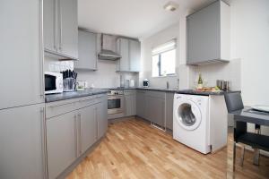 a kitchen with white cabinets and a washer and dryer at Dray Court - Luxury 2 Bedroom Apartment in Cardiff