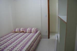 a bed in a white room with a purple comforter at Pousada Bem Brasil in Macaé
