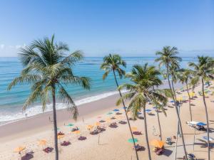 a beach with palm trees and umbrellas and the ocean at Hotel Brisa Tower Maceió in Maceió