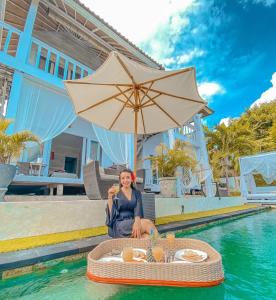 The Puncak Private Villa في نوسا ليمبونغان: امرأة جالسة في الماء بجانب طاولة مع مظلة