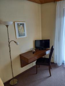 a room with a desk with a television and a lamp at Pension Grasy in Aidlingen