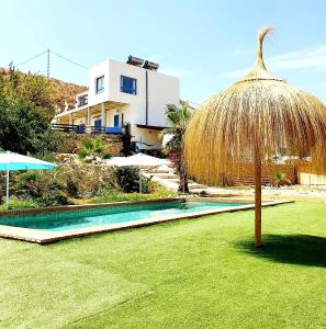 a swimming pool with a straw umbrella and a house at B&B La Nava Suites in Mojácar