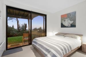 a bedroom with a bed and a large window at Skenes Beach House Stunning Ocean Views Amongst A Natural Bush Setting in Apollo Bay