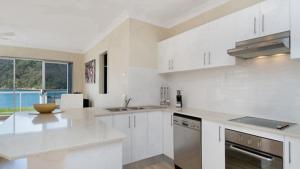 a kitchen with white cabinets and a large window at By The Beach - Waterfront Ettalong Beach in Ettalong Beach