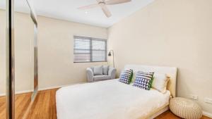 a white bedroom with a bed and a chair at Sea View - Ettalong Beach in Ettalong Beach