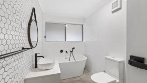 une salle de bain avec une baignoire, un lavabo et un miroir dans l'établissement Coastal Cottage - Ettalong Beach, à Ettalong Beach