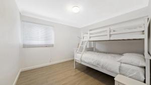 - une chambre blanche avec des lits superposés et une fenêtre dans l'établissement Coastal Cottage - Ettalong Beach, à Ettalong Beach