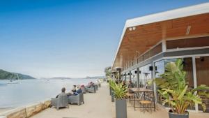 un bâtiment avec des personnes assises dans des chaises à côté de l'eau dans l'établissement Coastal Cottage - Ettalong Beach, à Ettalong Beach