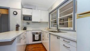 Lazy Days Seaside Cottage - Umina Beach في أومينا: مطبخ بخزائن بيضاء ومغسلة