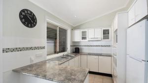 a kitchen with white cabinets and a clock on the wall at Beach Daze - Umina Beach Family Friendly in Umina
