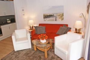 a living room with a red couch and two white chairs at Blockhaus mit W LAN sehr strandnah in Damp
