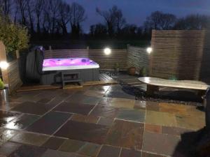 una bañera de hidromasaje y un banco en el patio por la noche en Moors Wood Relaxing ,Tranquil retreat with Hot Tub en Chippenham