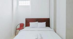 een witte slaapkamer met een bed en een rode stoel bij RedDoorz @ Tongas Probolinggo in Pesisir