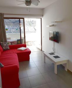 a living room with a red couch and a table at Tranquility Arimar Apartment Puerto Rico in Puerto Rico de Gran Canaria