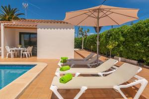 a villa with a swimming pool and lawn chairs and an umbrella at Villa Marina -Cala EnPorter- in Cala en Porter