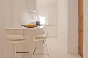 a white kitchen with two stools and a bowl of fruit at Studio cozy sur la Marina de Bonifacio in Bonifacio