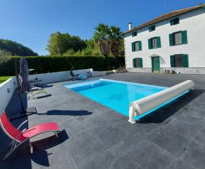 a swimming pool in front of a house with a red chair at Gite Moulin Urketa in Ayherre