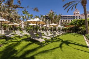 un groupe de chaises longues et de parasols sur une pelouse dans l'établissement Lopesan Costa Meloneras Resort & Spa, à Meloneras