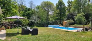 a backyard with a swimming pool and an umbrella at Jolie maison en pleine nature in Villiers-sous-Grez