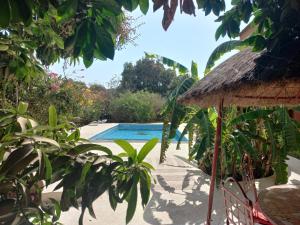 a resort with a swimming pool and a straw umbrella at Begue Pokai in Toubab Dialaw