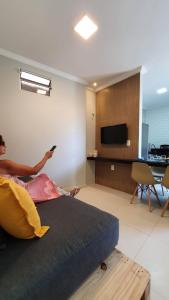 una persona está sentada en una cama en una sala de estar en Studio pé na areia com 2 quartos sala cozinha en Trairi