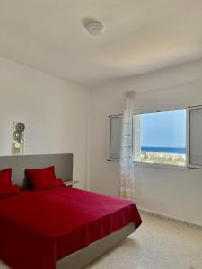 a white bedroom with a red bed and a window at Soltane Résidence in Hammamet