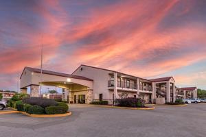 a large building with a cloudy sky in a parking lot at Best Western Lindale Inn in Lindale
