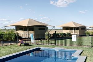 a swimming pool in front of a house with tents at Mitchell Grass Retreat in Longreach