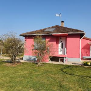 uma casa cor-de-rosa com um jardim de relva à frente. em Gîte de la Maison du L.A.C em Simard