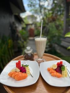 2 weiße Teller mit Obst und ein Getränk auf dem Tisch in der Unterkunft Taman Ayu Ubud in Ubud