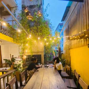 two people sitting at a wooden table in a courtyard at Chủ Nhật Cafe & Homestay - 12 ngõ 41 Đường Láng - Cơ sở 1 in Hanoi