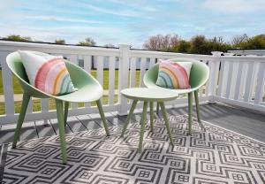 twee stoelen en een tafel op een veranda met een regenboogkussen bij Belle Aire Holiday Park in Hemsby