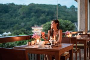 une femme assise à une table dans un restaurant dans l'établissement Mandarava Resort and Spa, Karon Beach - SHA Extra Plus, à Karon Beach