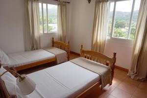 a bedroom with two beds and two windows at La Villa Therese in Anse Royale