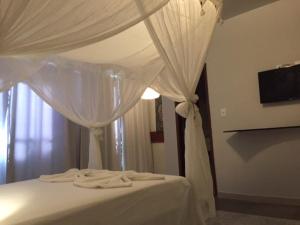 uma cama branca com um dossel com cortinas brancas em Pousada do Gunga em Barra de São Miguel