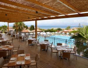 ein Restaurant mit Tischen und Stühlen sowie einem Pool in der Unterkunft Roda Beach Resort & Spa in Karousádes