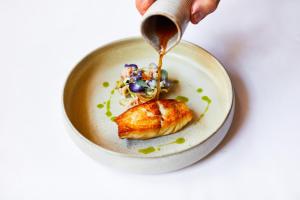 a person drizzling sauce onto a plate of food at ABode Canterbury in Canterbury