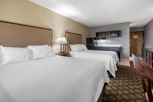 two beds in a hotel room with white sheets at Suburban Studios Lafayette in Lafayette