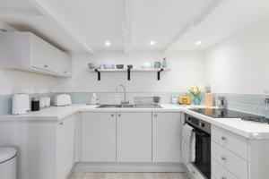 Biała kuchnia z białymi szafkami i zlewem w obiekcie Finest Retreats - Coral Cottage w mieście Porthleven
