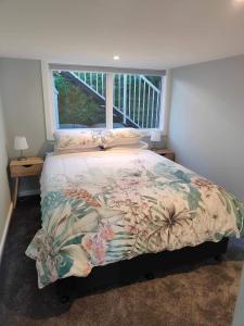 a bedroom with a bed with a floral comforter and a window at Fully Renovated Hillside Apartment Close To City in Christchurch