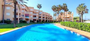 a swimming pool in front of a building with palm trees at Apartamento Flamingo by DENIA COSTA in Denia