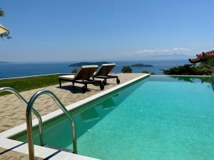 a swimming pool with two chairs and the ocean at Villa Azure in Skiathos