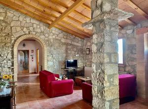 a living room with red chairs and a stone wall at Casa Rural Mas de les Àligues in Mequinenza