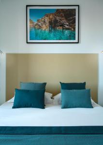 a bed with blue pillows and a picture on the wall at Hotel l'Isolella in Porticcio