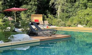 a deck with a chair and an umbrella next to a swimming pool at Bayern Resort Hotel - Adults only - mit Zugspitzblick - Eibsee-Nähe - Wellnessbereich - Naturpool im Sommer in Grainau